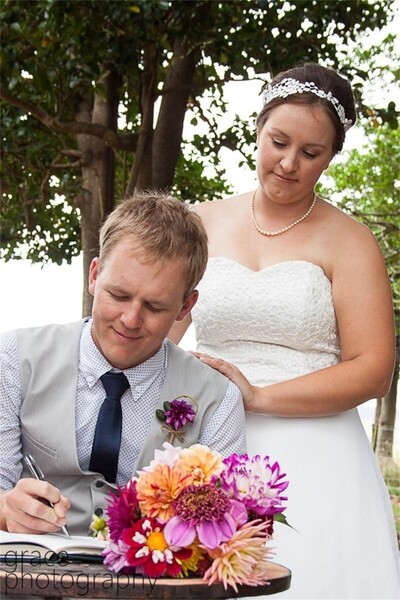 Groom signing register with flowers beside and bride standing beside